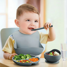 Load image into Gallery viewer, Baby eating with a bowl and spoon, wearing a bib, with text in the background